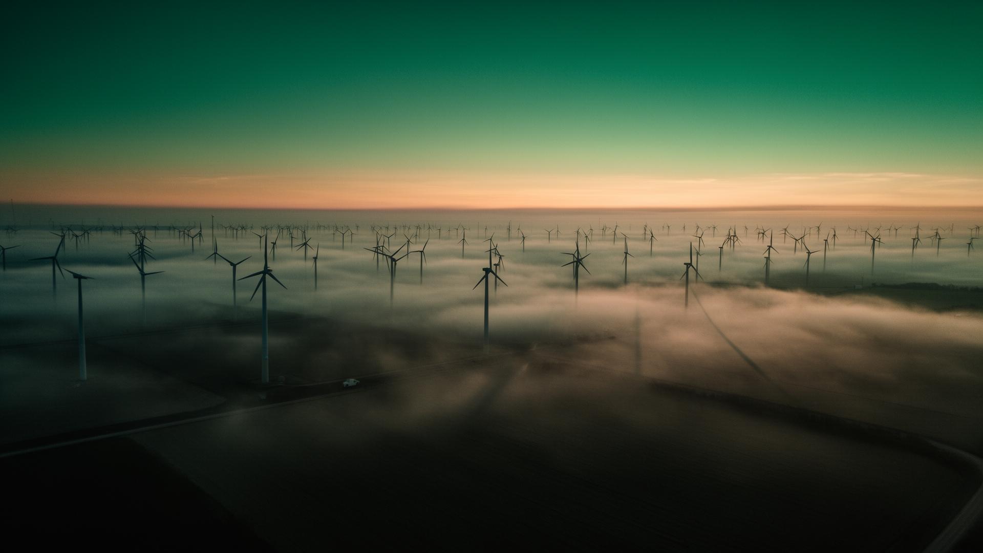 Wind turbines emerging through morning fog at dawn